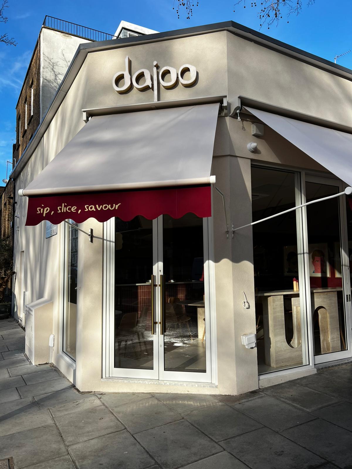 Dajoo daytime exterior — corner storefront with beige awning over a scalloped burgundy valance reading 'sip, slice, savour' in gold script