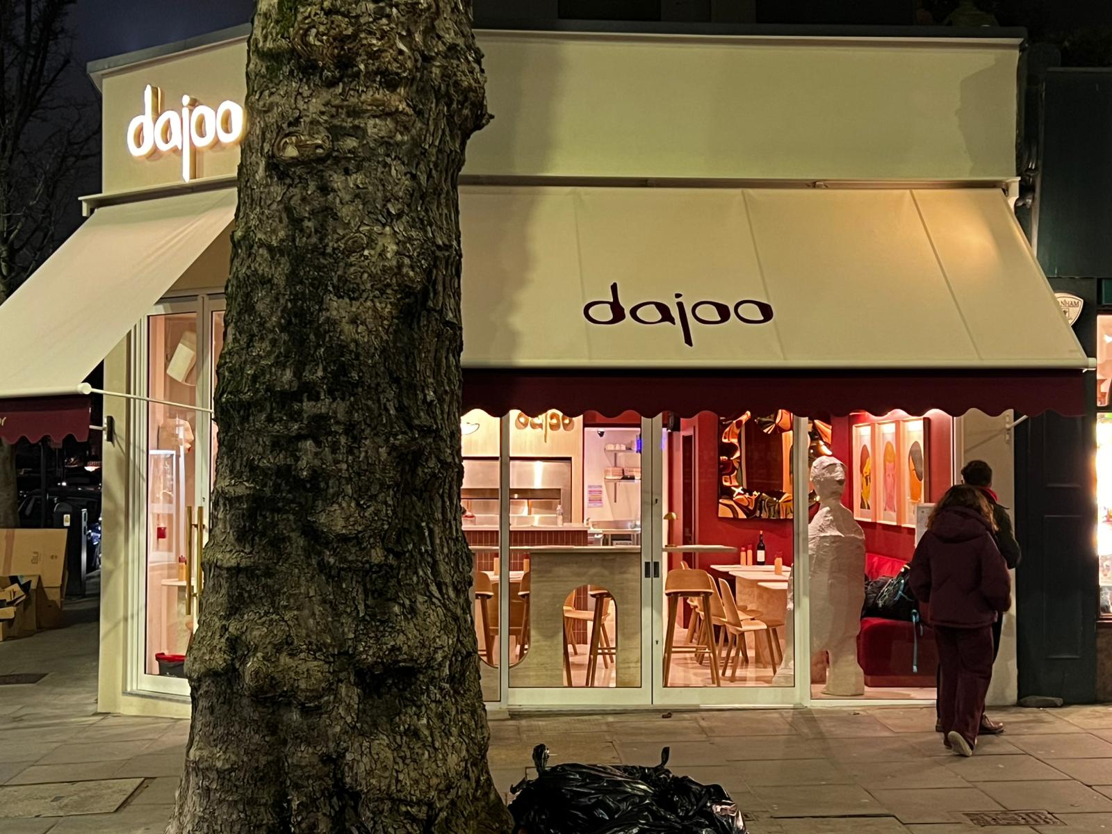 Dajoo at night through the window — lit interior with portrait art, plaster sculpture and warm burgundy walls