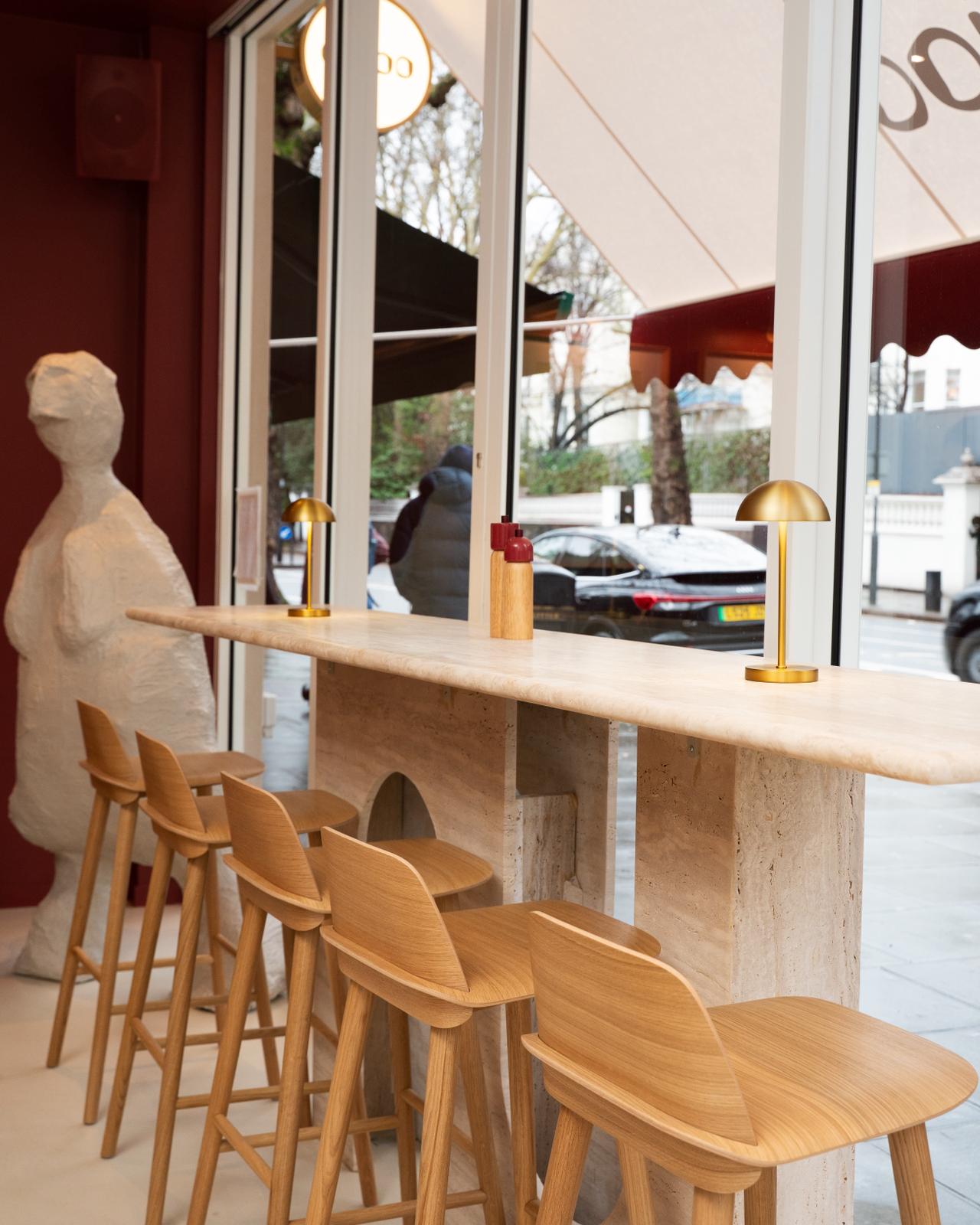 Dajoo travertine bar counter with oak stools, brass mushroom lamps, a plaster sculpture and a window onto the street