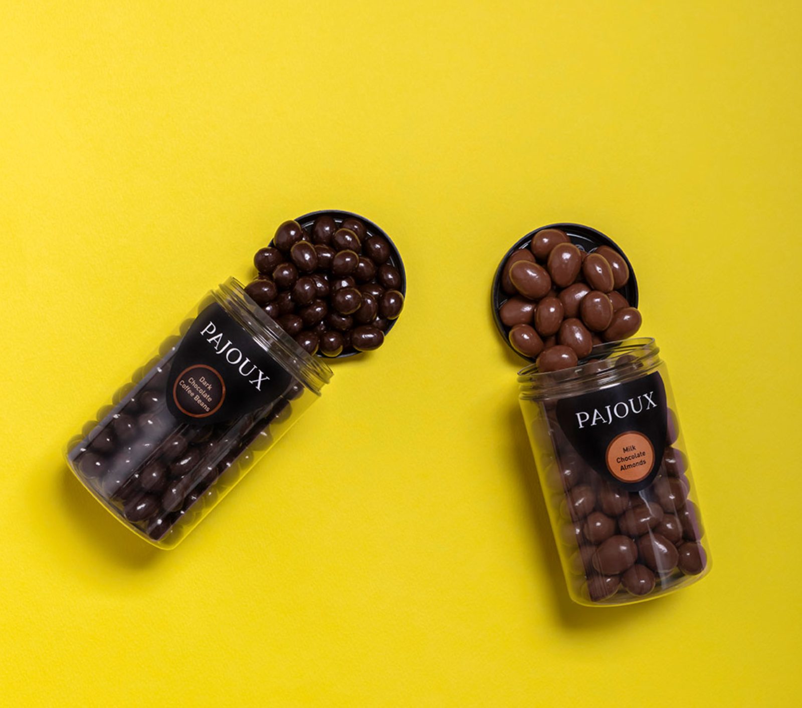 Two Pajoux jars of dark-chocolate coffee beans and milk-chocolate almonds on a saturated saffron yellow set